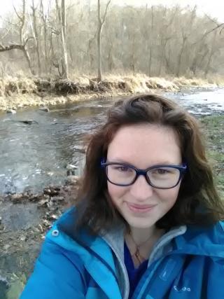 Headshot of Dr. Rejanne Le Bivic (She has on glasses, a blue jacket and is standing in front of a river)
